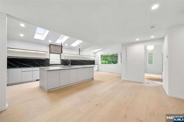 kitchen featuring modern cabinets, light wood-style floors, a skylight, white cabinets, and open floor plan