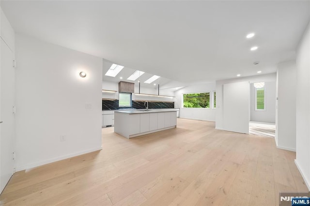 unfurnished living room with a sink, light wood finished floors, recessed lighting, baseboards, and a skylight