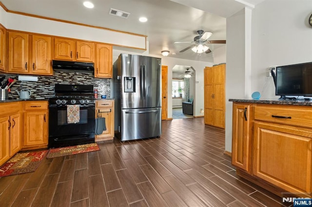kitchen featuring stainless steel fridge with ice dispenser, black gas range oven, a ceiling fan, under cabinet range hood, and decorative backsplash