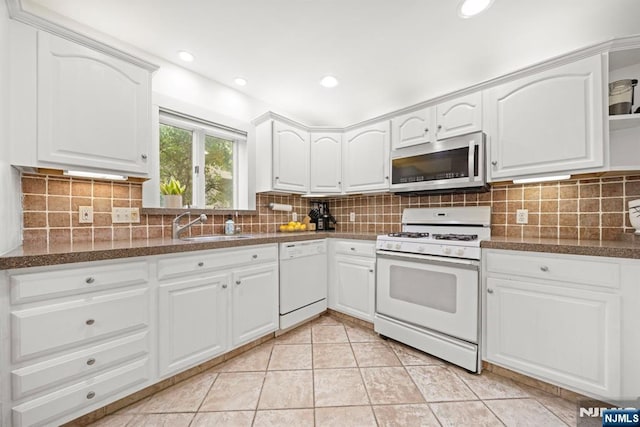 kitchen featuring white appliances, a sink, dark countertops, white cabinetry, and recessed lighting