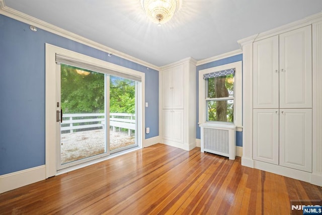 empty room featuring radiator heating unit, plenty of natural light, wood-type flooring, baseboards, and crown molding