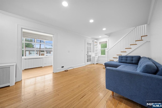 living area featuring radiator, stairway, crown molding, light wood finished floors, and recessed lighting