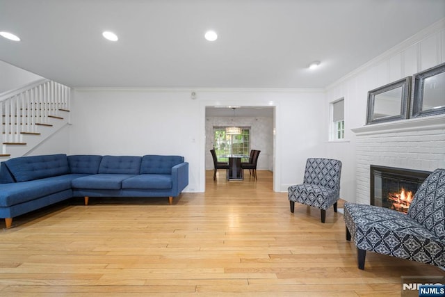 living room with ornamental molding, light wood finished floors, stairs, a fireplace, and recessed lighting