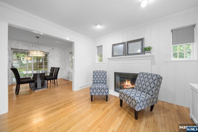 sitting room with light wood-type flooring, crown molding, a decorative wall, and a brick fireplace