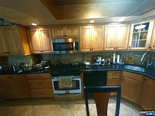 kitchen with stainless steel appliances, a sink, backsplash, dark countertops, and brown cabinets