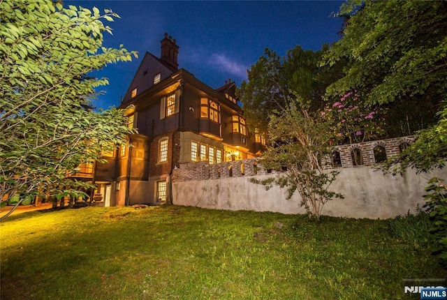 back of house at night featuring a lawn, a chimney, and stucco siding