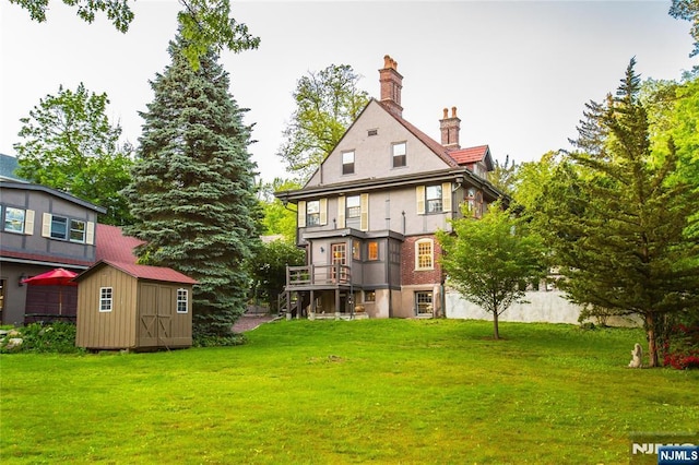 back of property with a shed, an outbuilding, a lawn, a chimney, and stairway