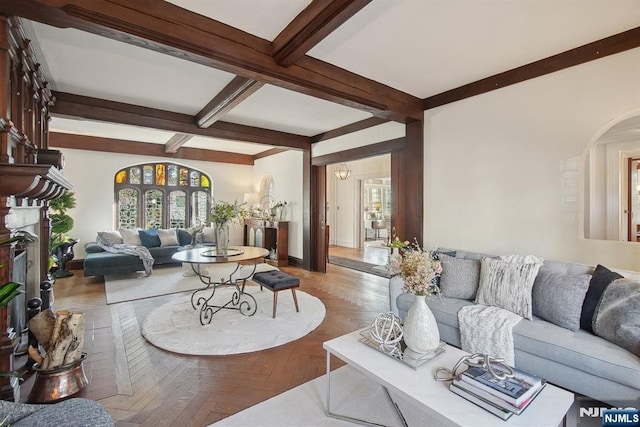 living area featuring arched walkways, beam ceiling, a fireplace with raised hearth, coffered ceiling, and baseboards
