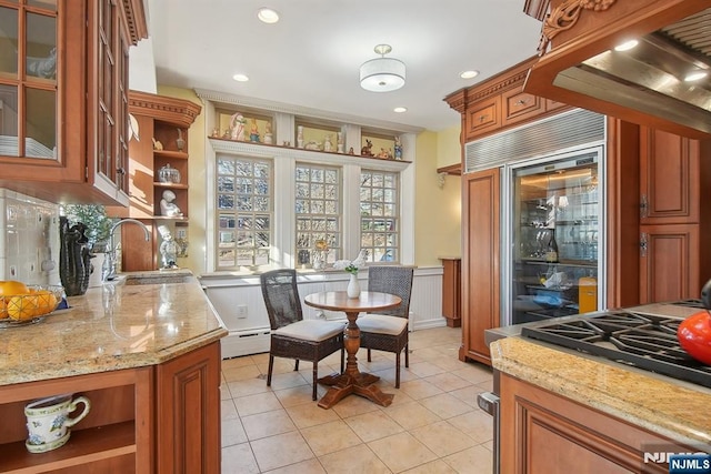 kitchen featuring open shelves, brown cabinets, a sink, light stone countertops, and wainscoting