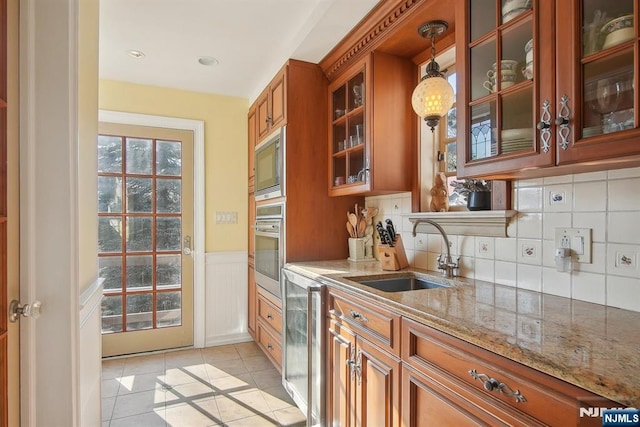 kitchen featuring a sink, appliances with stainless steel finishes, brown cabinets, light stone countertops, and light tile patterned floors