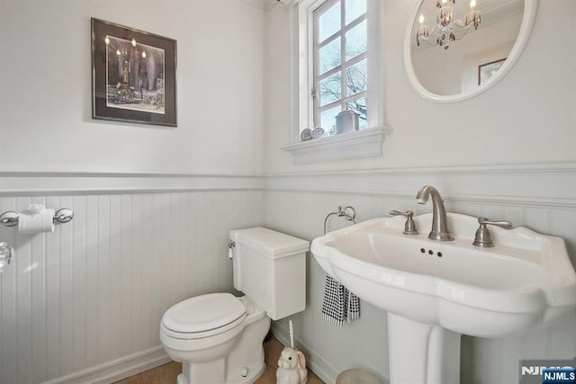 half bath with a wainscoted wall, toilet, a sink, and a chandelier