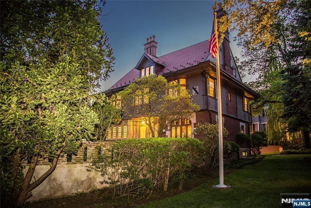 back of property featuring a chimney, a yard, brick siding, and stucco siding