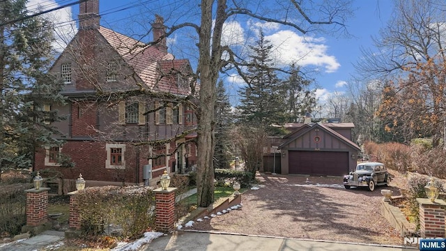 view of side of home featuring brick siding, dirt driveway, a garage, board and batten siding, and a chimney