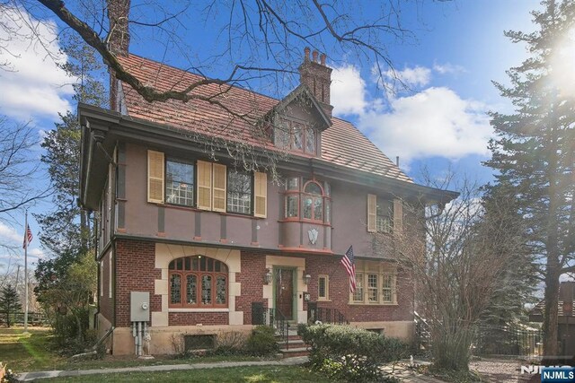 view of front facade with stucco siding, a chimney, and brick siding