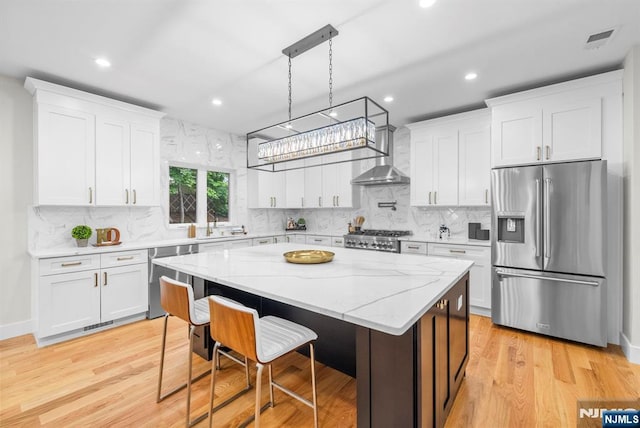 kitchen featuring appliances with stainless steel finishes, wall chimney range hood, light wood finished floors, white cabinets, and recessed lighting