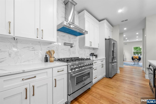 kitchen with premium appliances, wall chimney range hood, white cabinetry, backsplash, and recessed lighting