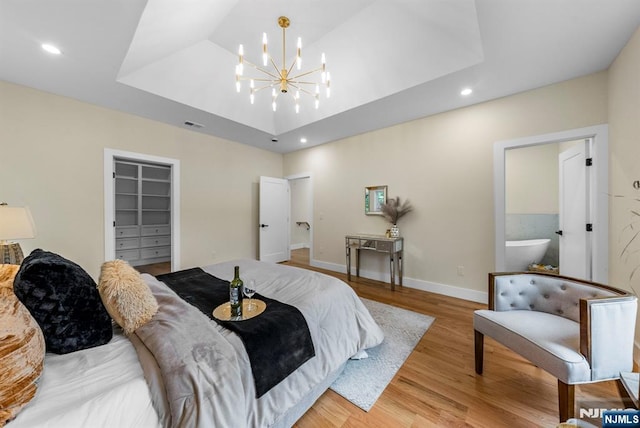bedroom featuring a raised ceiling, light wood-style floors, recessed lighting, a chandelier, and a spacious closet