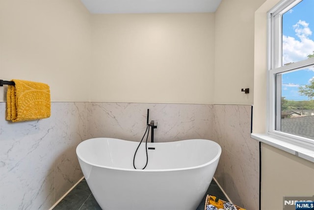 bathroom with a freestanding bath, a wainscoted wall, and tile walls