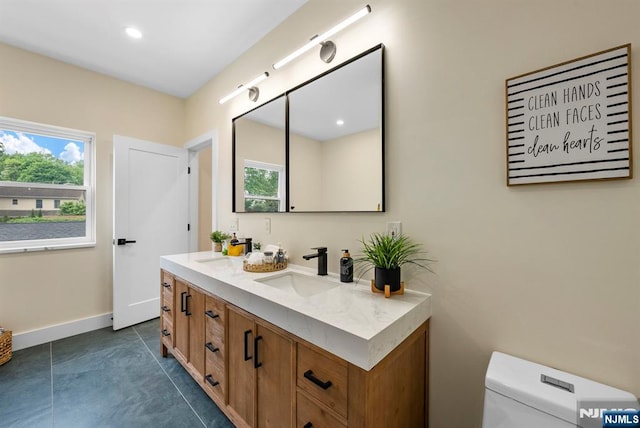 bathroom with healthy amount of natural light, baseboards, double vanity, toilet, and recessed lighting