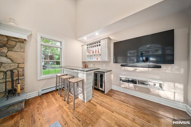 17 Sunset Ln, Upper Saddle River, NJ 07458 - indoor wet bar featuring baseboards, light wood-style floors, a baseboard radiator, a high ceiling, and wine cooler