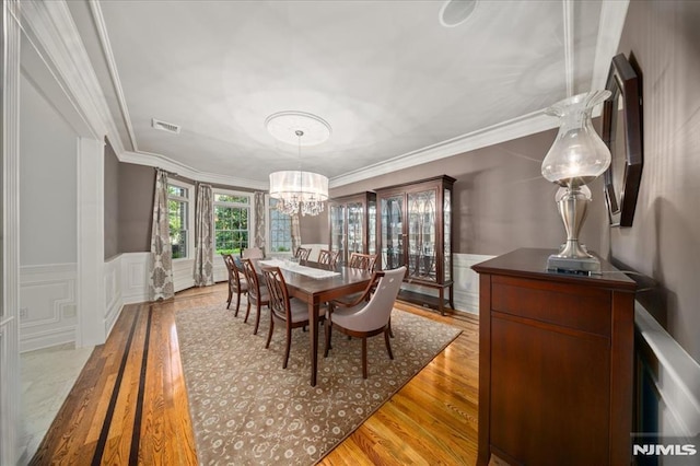 17 Sunset Ln, Upper Saddle River, NJ 07458 - dining space with light wood-style flooring, a chandelier, crown molding, a wainscoted wall, and a decorative wall