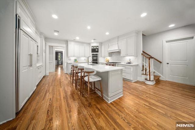 17 Sunset Ln, Upper Saddle River, NJ 07458 - kitchen featuring oven, a kitchen breakfast bar, light countertops, a kitchen island with sink, and white cabinets