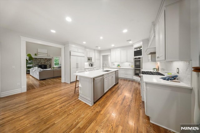 17 Sunset Ln, Upper Saddle River, NJ 07458 - kitchen featuring appliances with stainless steel finishes, a sink, a center island with sink, light countertops, and light wood-style flooring