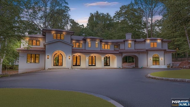 view of front of home featuring a chimney, driveway, stucco siding, covered porch, and a tile roof