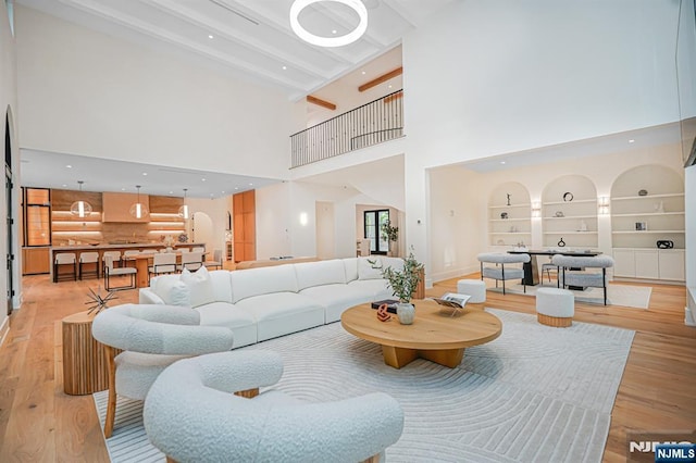 living area with light wood-style floors, a towering ceiling, baseboards, beamed ceiling, and built in features