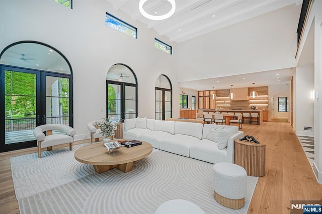 living area with light wood finished floors, french doors, a towering ceiling, beam ceiling, and baseboards