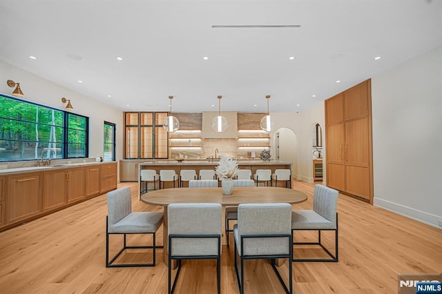 dining space with light wood-type flooring, recessed lighting, baseboards, and arched walkways