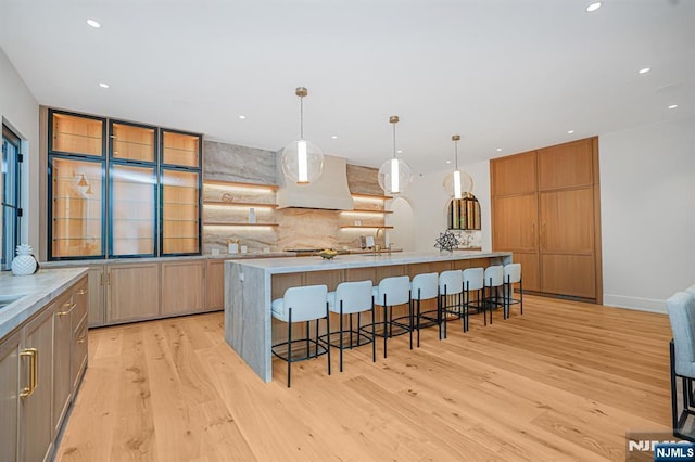 kitchen with extractor fan, light wood finished floors, backsplash, a kitchen breakfast bar, and recessed lighting
