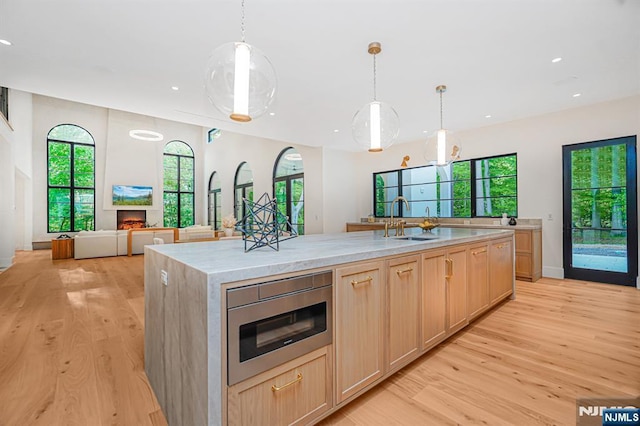 kitchen featuring a sink, light wood-style flooring, a lit fireplace, an island with sink, and recessed lighting