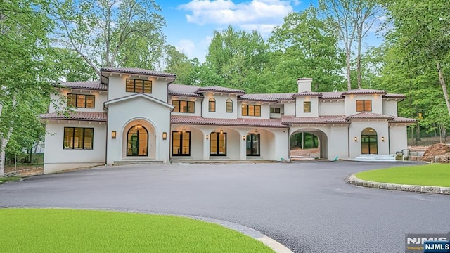 mediterranean / spanish-style home with a chimney, stucco siding, a porch, and asphalt driveway