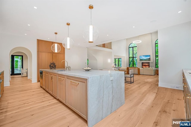 kitchen with a sink, arched walkways, light wood-type flooring, recessed lighting, and light stone countertops