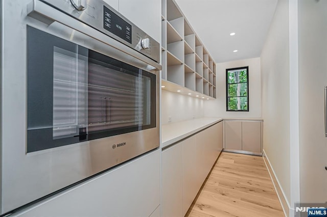 kitchen with light wood-type flooring, open shelves, double oven, light countertops, and recessed lighting