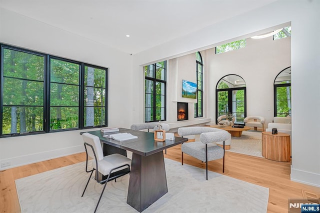 office area featuring a warm lit fireplace, light wood-type flooring, and baseboards
