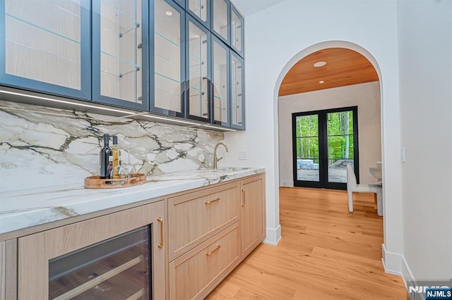 bar area with light wood-style flooring, decorative backsplash, a sink, arched walkways, and baseboards