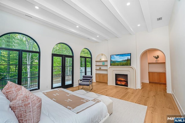 bedroom with beamed ceiling, light wood-style flooring, recessed lighting, a warm lit fireplace, and arched walkways