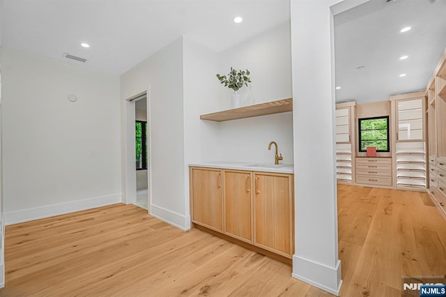 bar featuring light wood-type flooring, a sink, recessed lighting, and baseboards