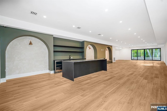unfurnished living room featuring light wood finished floors, wine cooler, baseboards, arched walkways, and recessed lighting