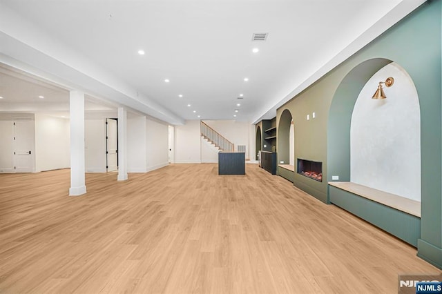 unfurnished living room with recessed lighting, stairway, light wood-style floors, a lit fireplace, and baseboards
