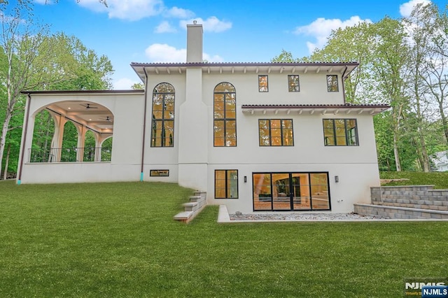 back of house with a chimney, a lawn, stucco siding, and a ceiling fan