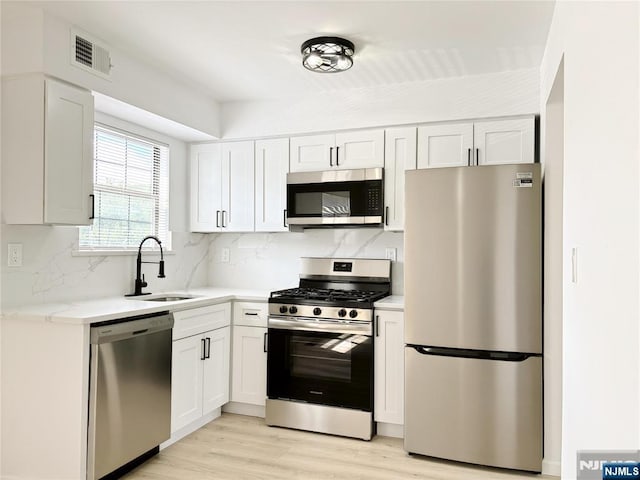 kitchen with appliances with stainless steel finishes, a sink, backsplash, light wood-type flooring, and white cabinetry