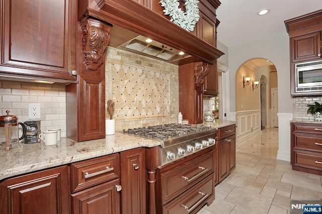 7 Newton Pl, Allendale, NJ 07401 - kitchen with stainless steel appliances, arched walkways, a wainscoted wall, light stone countertops, and backsplash