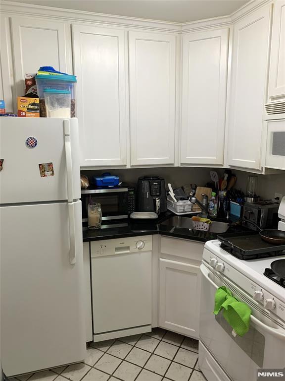 116 W 19th St Unit 1A, Bayonne, NJ 07002 - kitchen featuring white appliances, white cabinets, light tile patterned flooring, and dark countertops