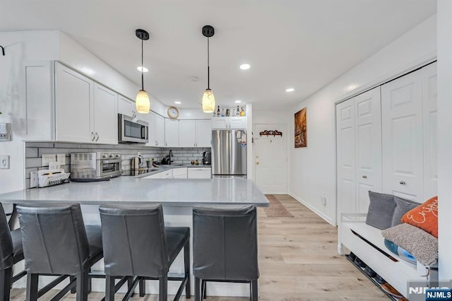 kitchen featuring appliances with stainless steel finishes, a peninsula, light wood-style flooring, white cabinetry, and recessed lighting
