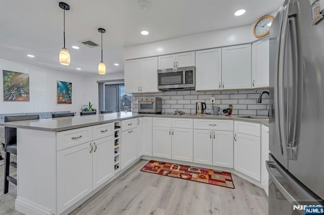 kitchen featuring appliances with stainless steel finishes, a sink, a peninsula, light wood-style flooring, and recessed lighting