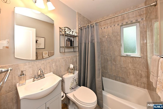 bathroom with vanity, shower / bathtub combination with curtain, tile walls, toilet, and wainscoting