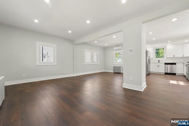 240 Berry St, Hackensack, NJ 07601 - unfurnished living room with radiator heating unit, healthy amount of natural light, a wall mounted air conditioner, dark wood-type flooring, and recessed lighting